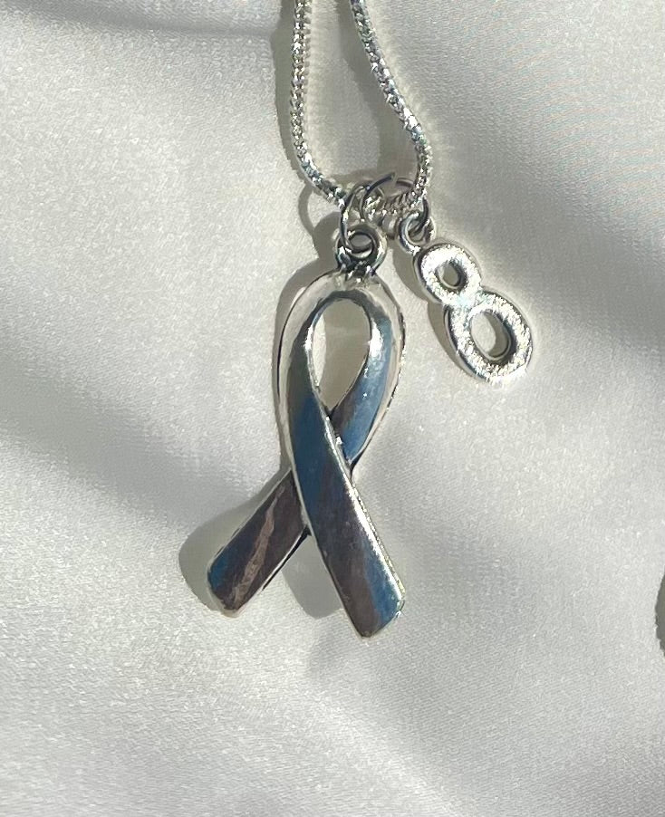 Silver ribbon charm necklace with number 8 on a white satin background