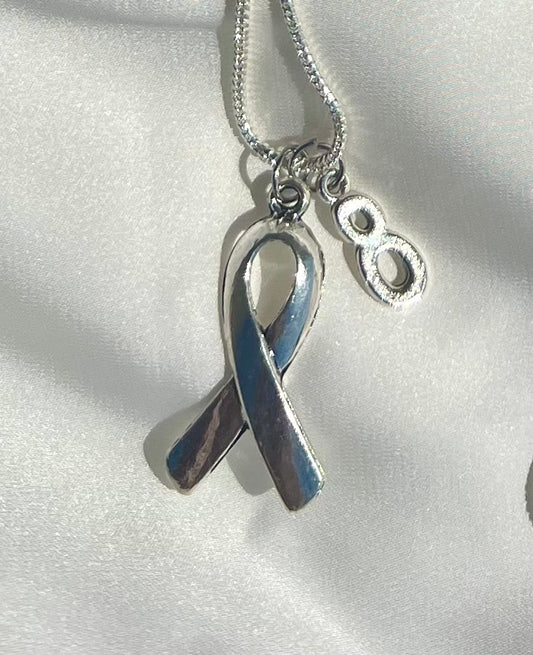 Silver ribbon charm necklace with number 8 on a white satin background